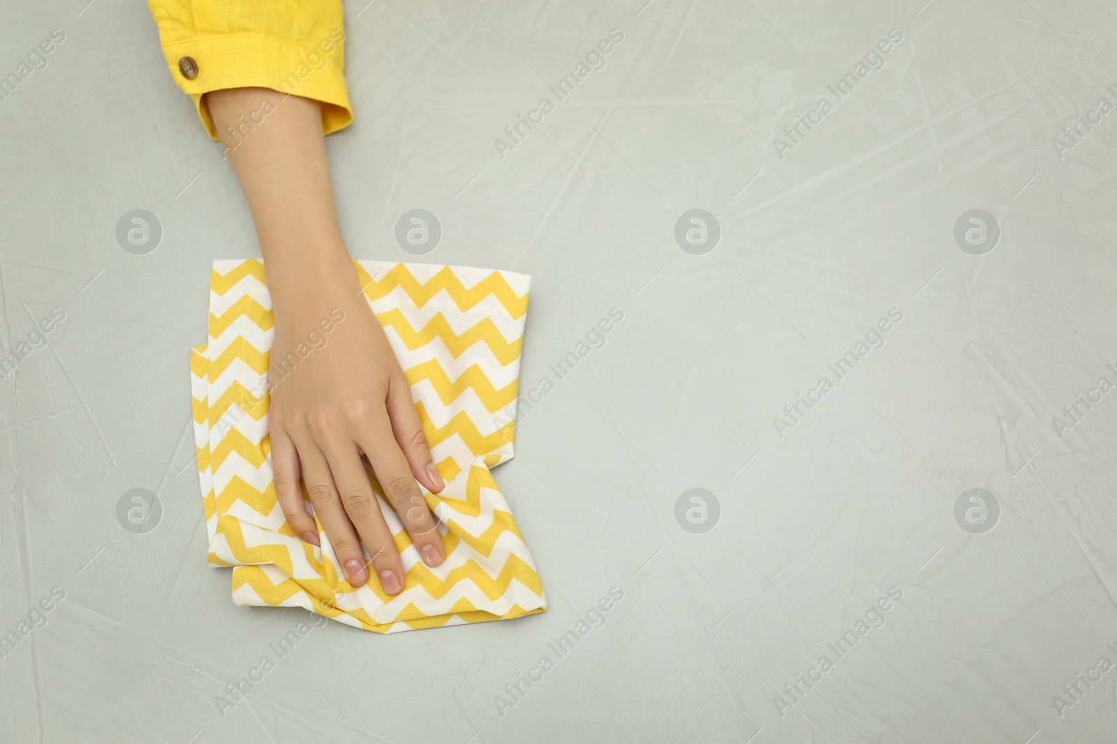 Photo of Woman wiping grey table with kitchen towel, top view. Space for text