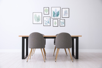 Photo of Stylish room interior with modern table, chairs and paintings of tropical leaves. Idea for design