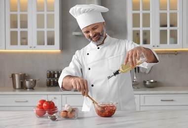 Photo of Professional chef pouring oil from bottle into delicious tomato sauce at white marble table indoors