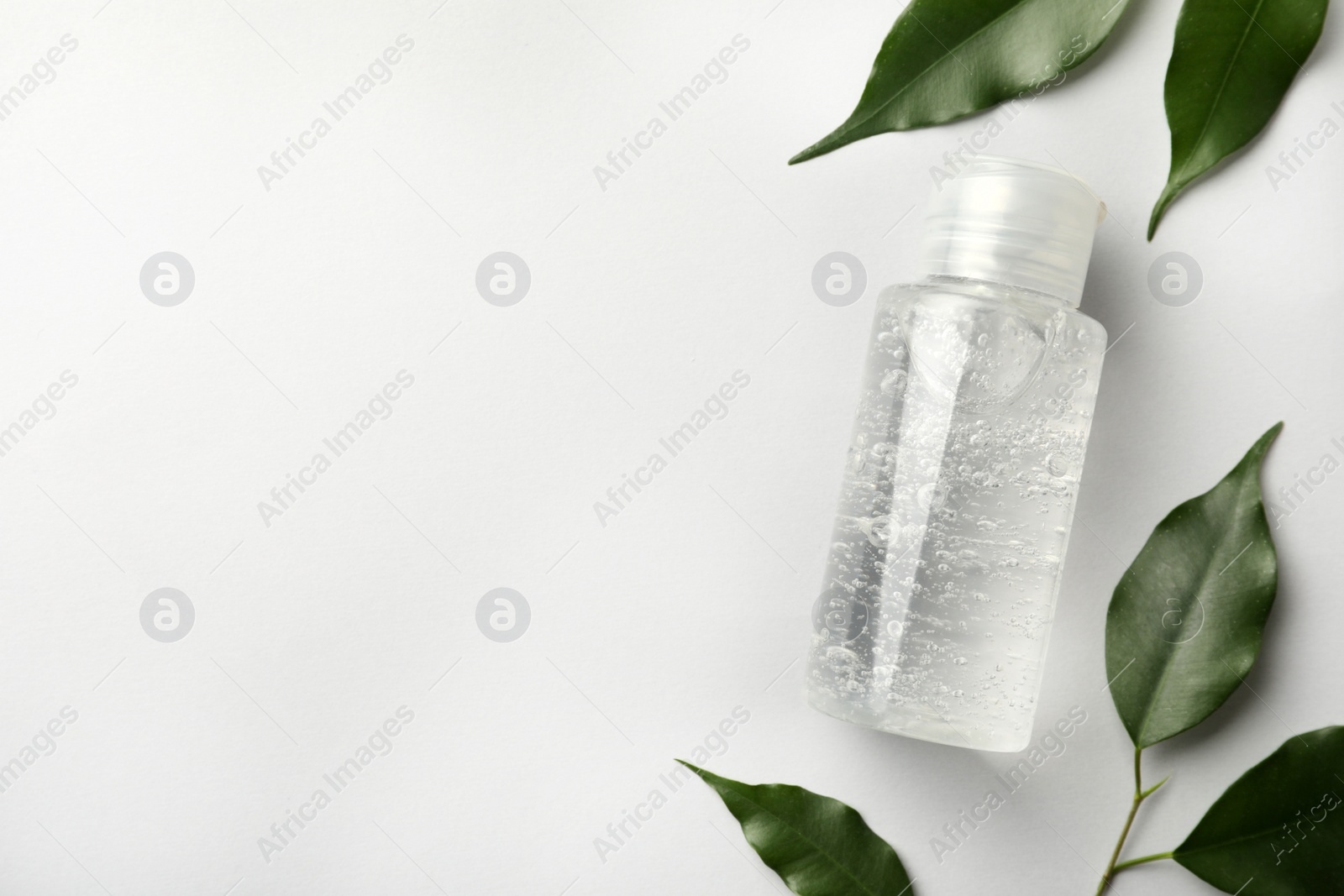 Photo of Bottle of cosmetic gel and green leaves on white background, flat lay. Space for text