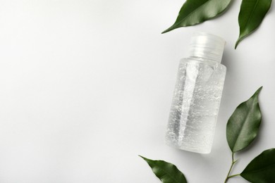 Bottle of cosmetic gel and green leaves on white background, flat lay. Space for text