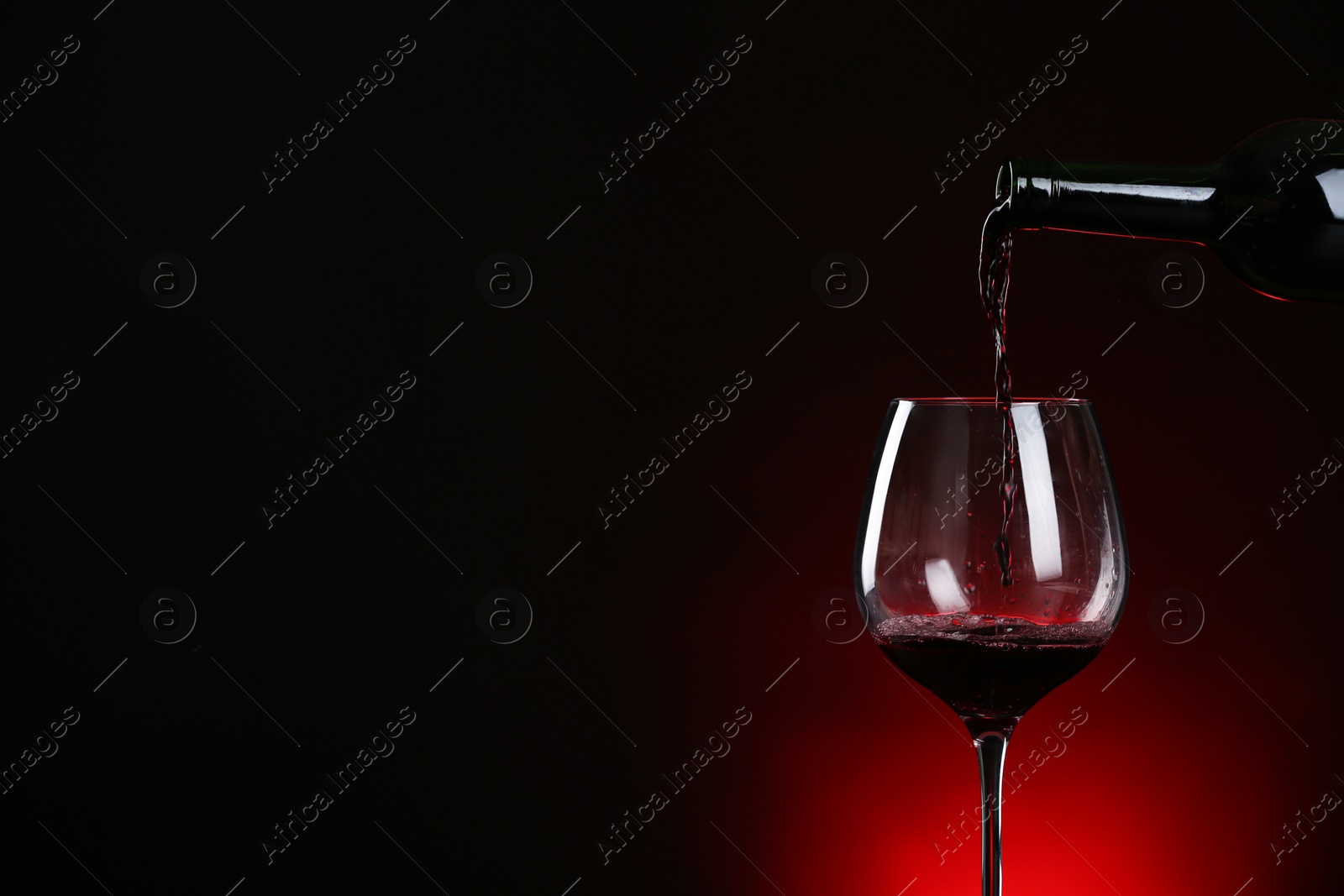 Photo of Pouring wine from bottle into glass on dark background, space for text