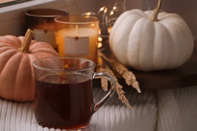 Photo of Cup of hot drink, candles and pumpkins on window sill indoors