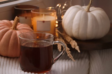 Cup of hot drink, candles and pumpkins on window sill indoors