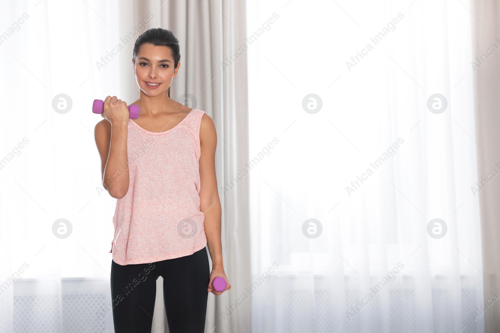 Photo of Young woman in fitness clothes doing exercise with dumbbells at home. Space for text