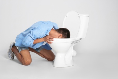 Photo of Young man vomiting in toilet bowl on gray background