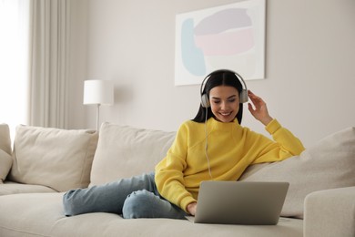 Photo of Woman with laptop and headphones sitting on sofa at home