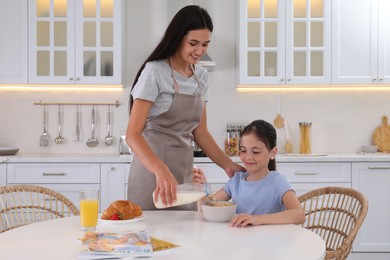 Photo of Happy mother adding milk to her daughter's cereal in kitchen. Single parenting