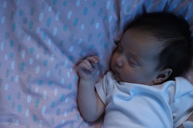 Cute newborn baby sleeping in crib at night, top view