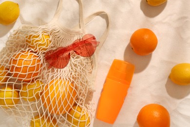 Photo of String bag with sunglasses, fruits and sunscreen on sand, flat lay