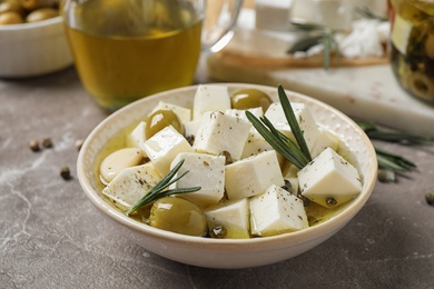 Composition with pickled feta cheese in bowl on light brown table