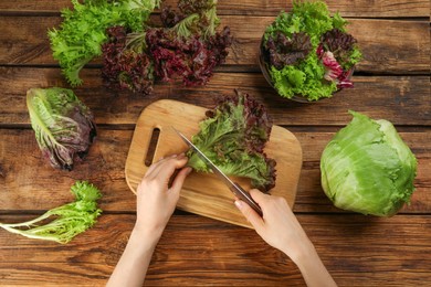 Photo of Woman cutting red leaf lettuce at wooden table, top view