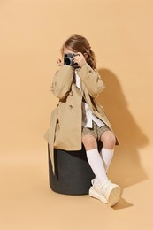 Fashion concept. Stylish girl with vintage camera on pale orange background