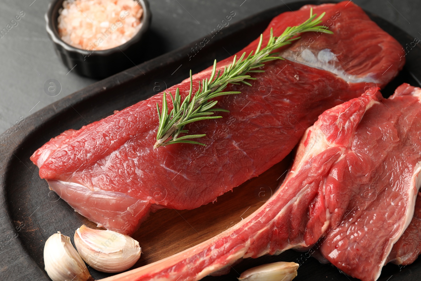 Photo of Pieces of raw beef meat and spices on grey table, closeup