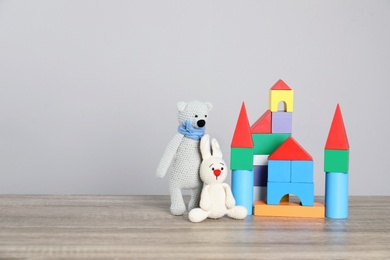 Cute toys and castle made of colorful blocks on table against light background, space for text. Child room elements