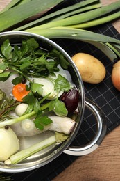 Photo of Pot and different ingredients for cooking tasty bouillon on wooden table, flat lay