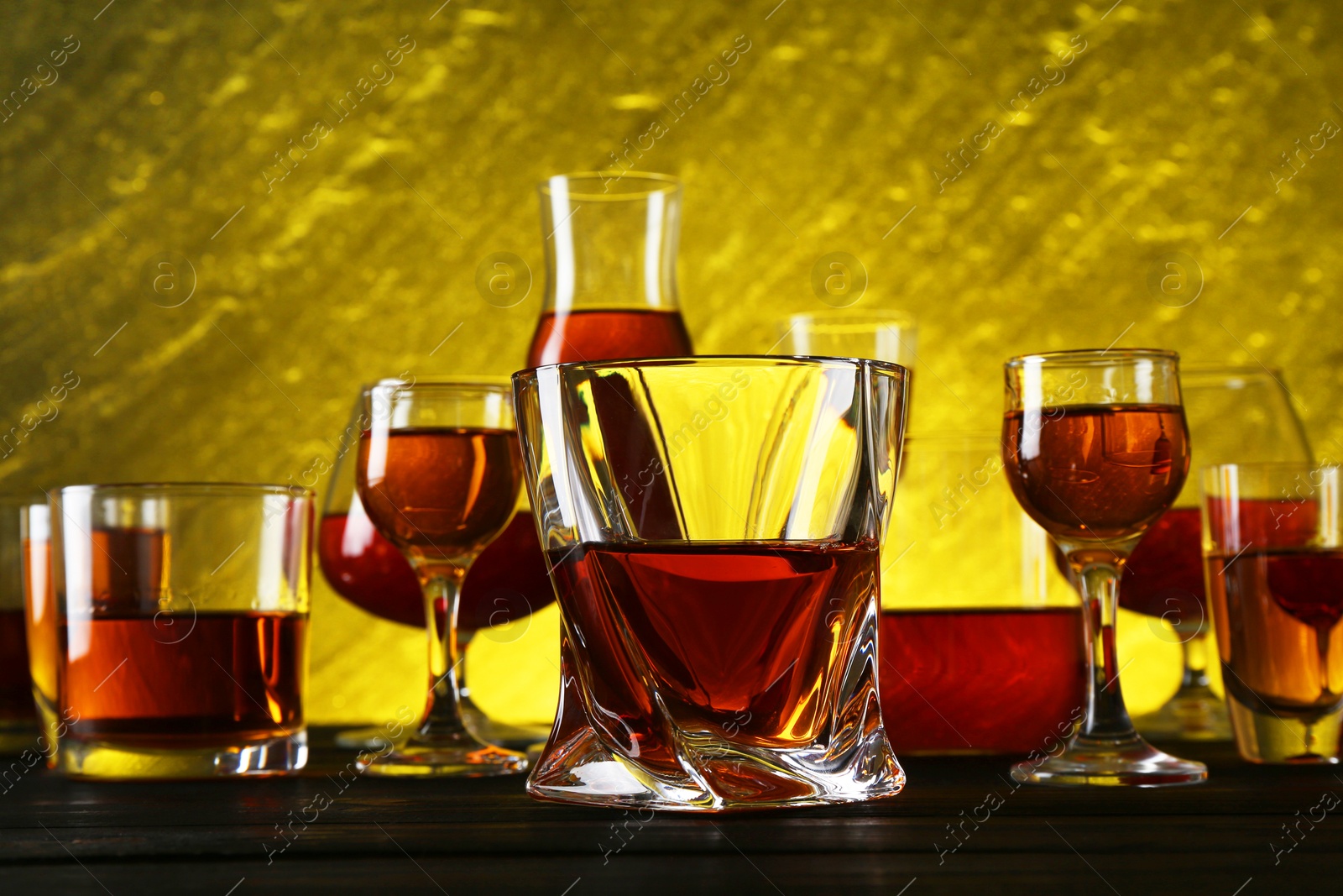 Photo of Different delicious liqueurs in glasses on dark wooden table