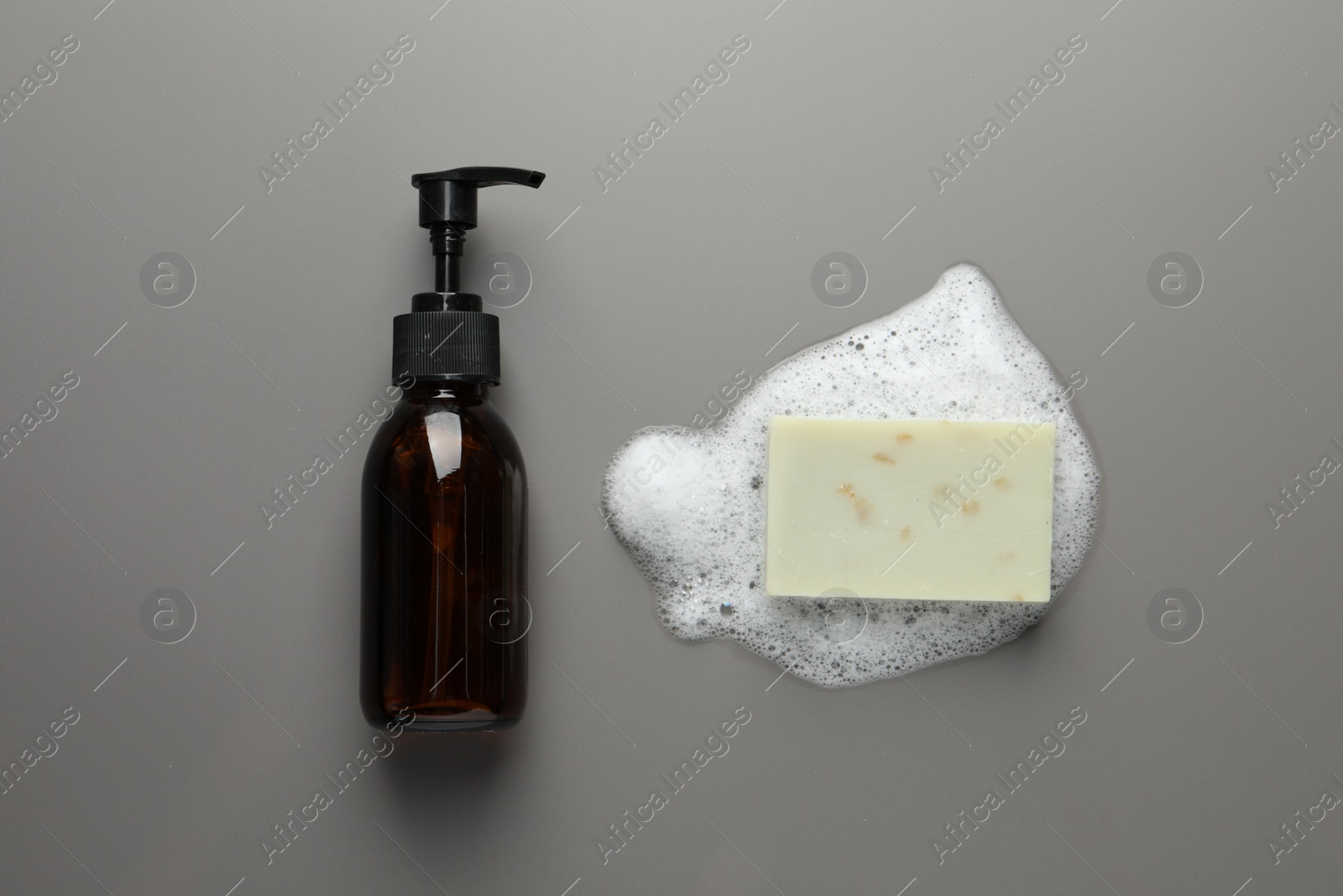 Photo of Dispenser and soap bar with fluffy foam on grey background, flat lay