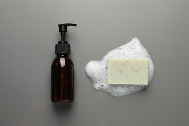 Dispenser and soap bar with fluffy foam on grey background, flat lay