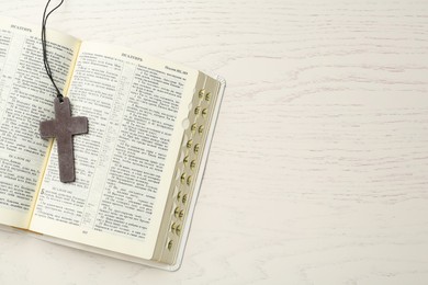 MYKOLAIV, UKRAINE - DECEMBER 20, 2021: Christian cross and Bible on white wooden table, top view. Space for text