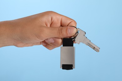 Photo of Woman holding key with keychain on light blue background, closeup