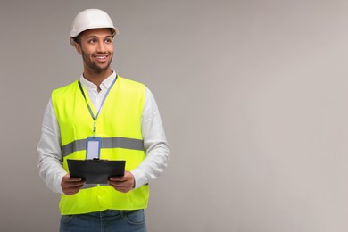 Engineer in hard hat holding clipboard on grey background, space for text