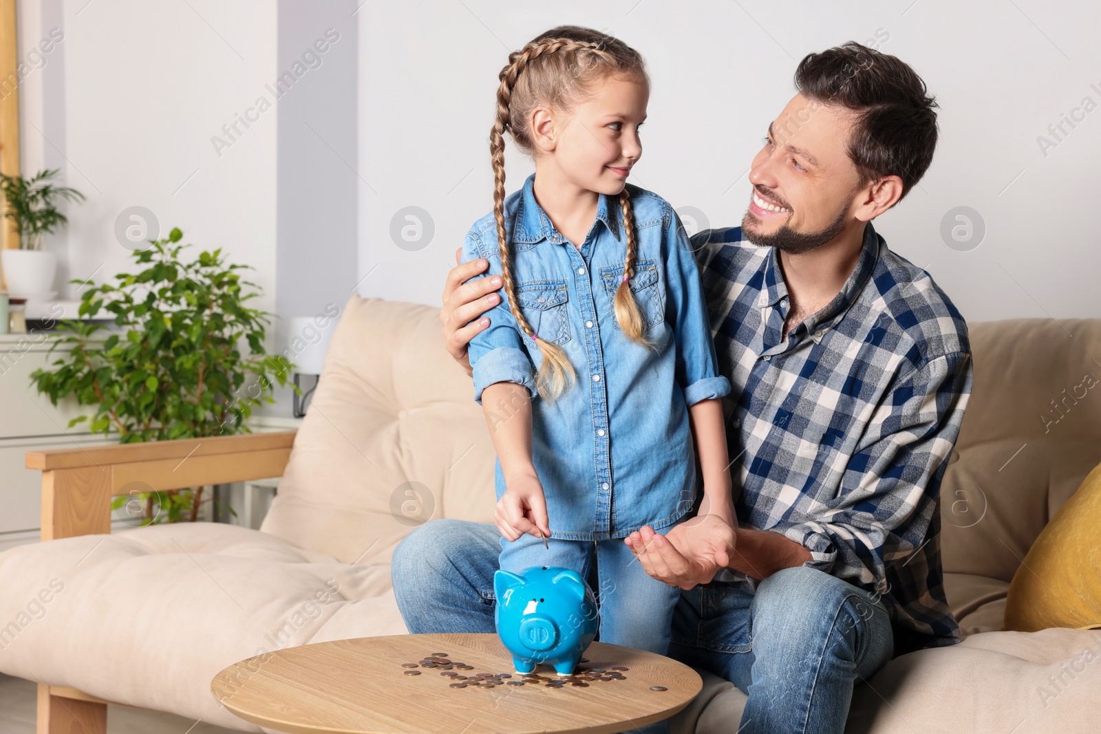 Photo of Little girl with her father putting coin into piggy bank at home