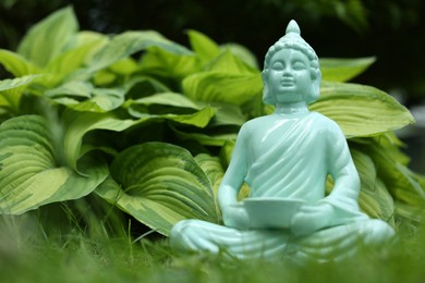 Photo of Decorative Buddha statue on green grass outdoors, closeup. Space for text