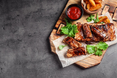 Delicious grilled ribs and garnish on grey table, top view. Space for text