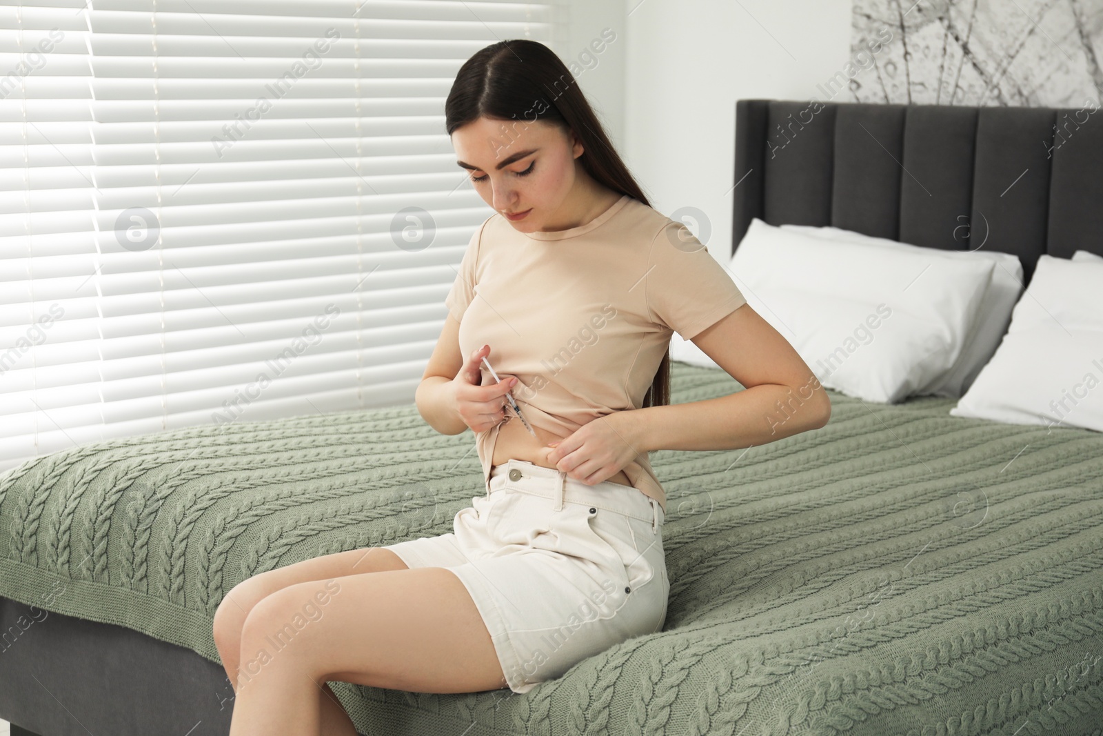 Photo of Diabetes. Woman making insulin injection into her belly on bed in room