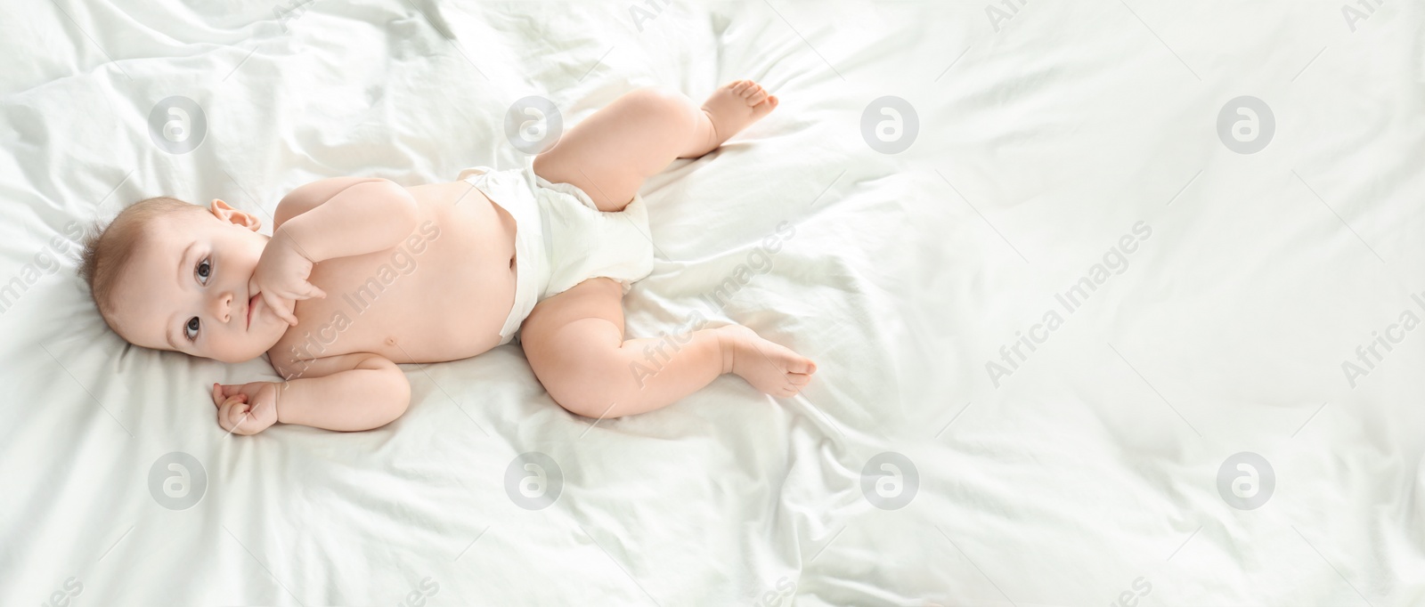 Image of Cute little baby in diaper lying on bed, above view with space for text. Banner design