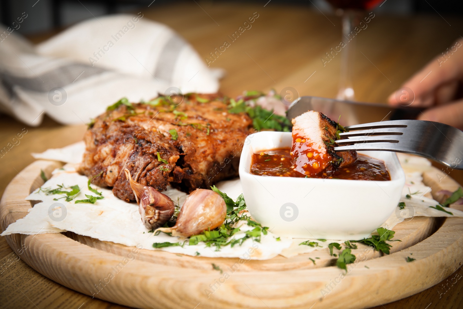 Photo of Woman eating delicious grilled pork chop at wooden table, closeup