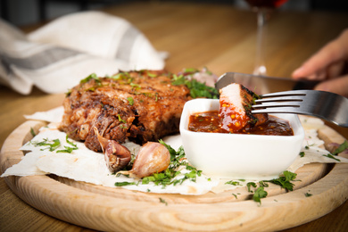 Photo of Woman eating delicious grilled pork chop at wooden table, closeup