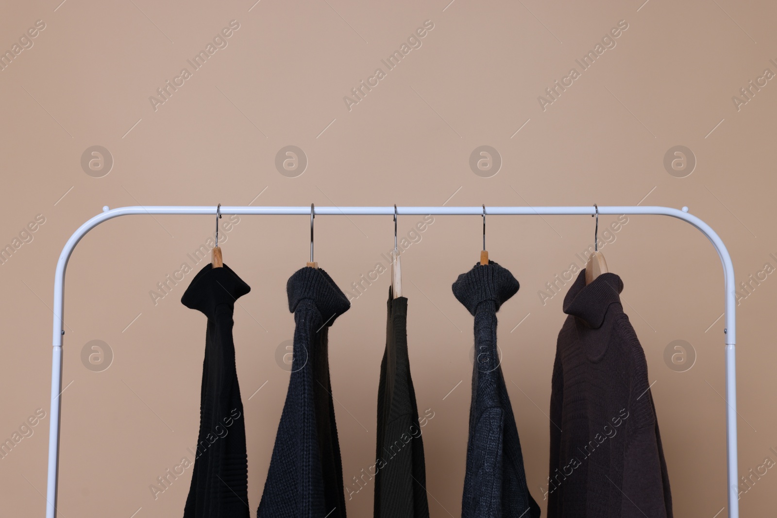 Photo of Rack with different warm sweaters on beige background