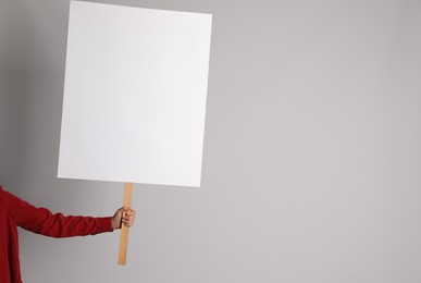 Photo of Woman holding blank sign on light grey background, closeup. Space for design