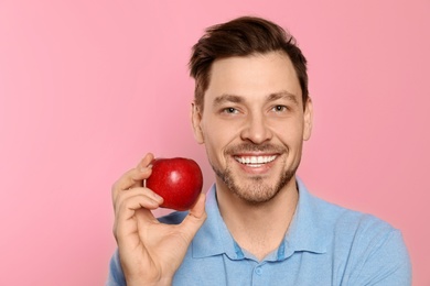 Photo of Smiling man with perfect teeth and red apple on color background