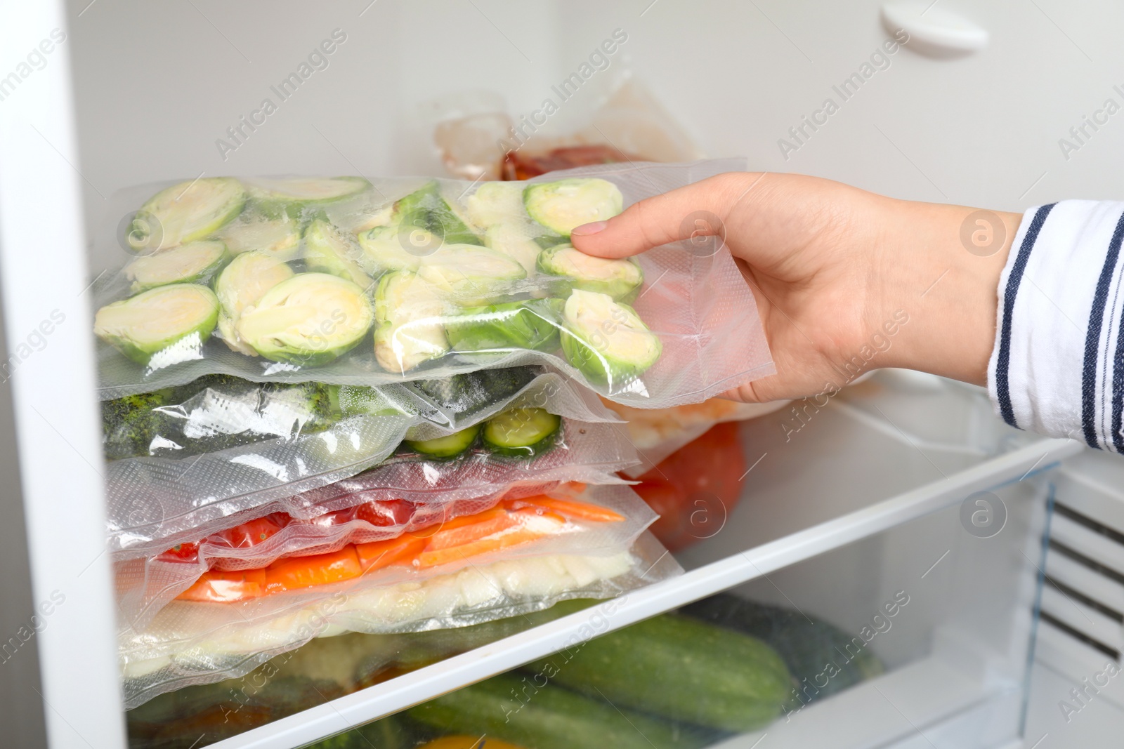 Photo of Woman putting vacuum bags with vegetables into fridge, closeup. Food storage