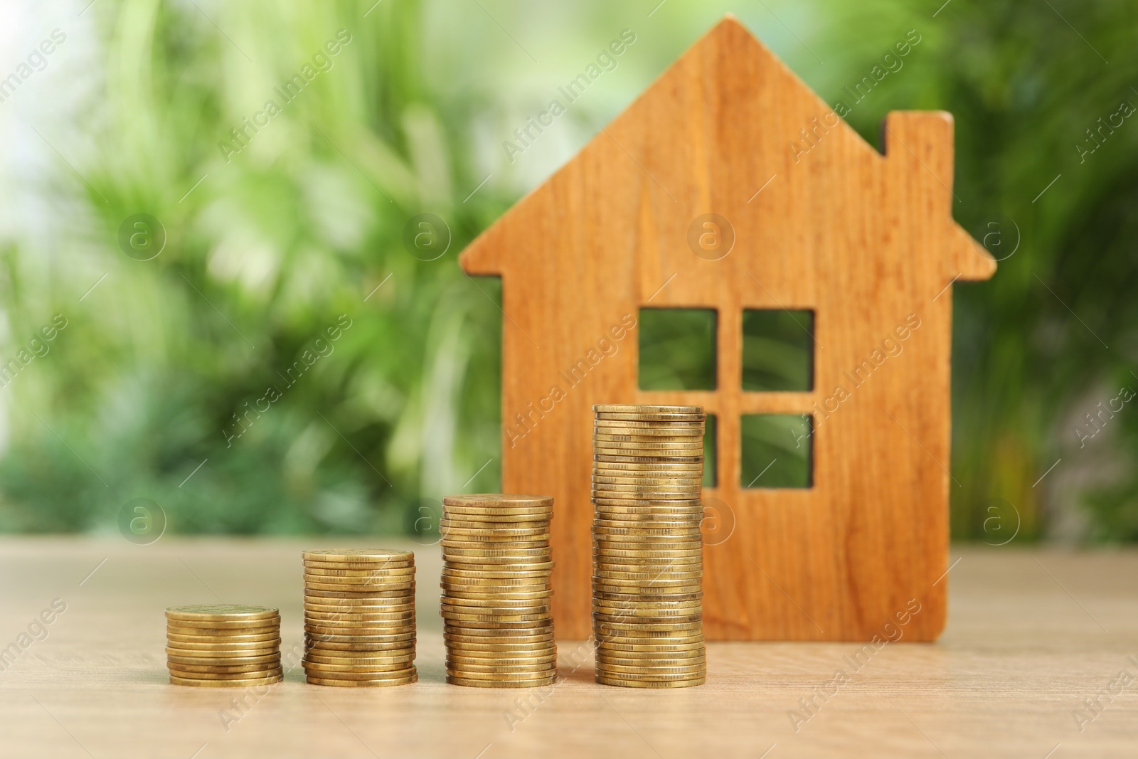 Photo of Mortgage concept. Model house and stacks of coins on wooden table against blurred green background