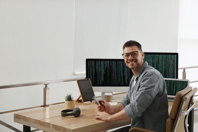 Photo of Happy programmer with smartphone working at desk in office