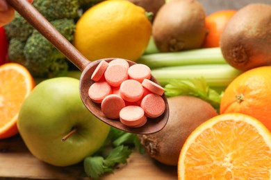 Photo of Dietary supplements. Spoon with pills over food products at table, closeup