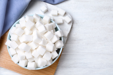 Refined sugar cubes on white wooden table, flat lay. Space for text