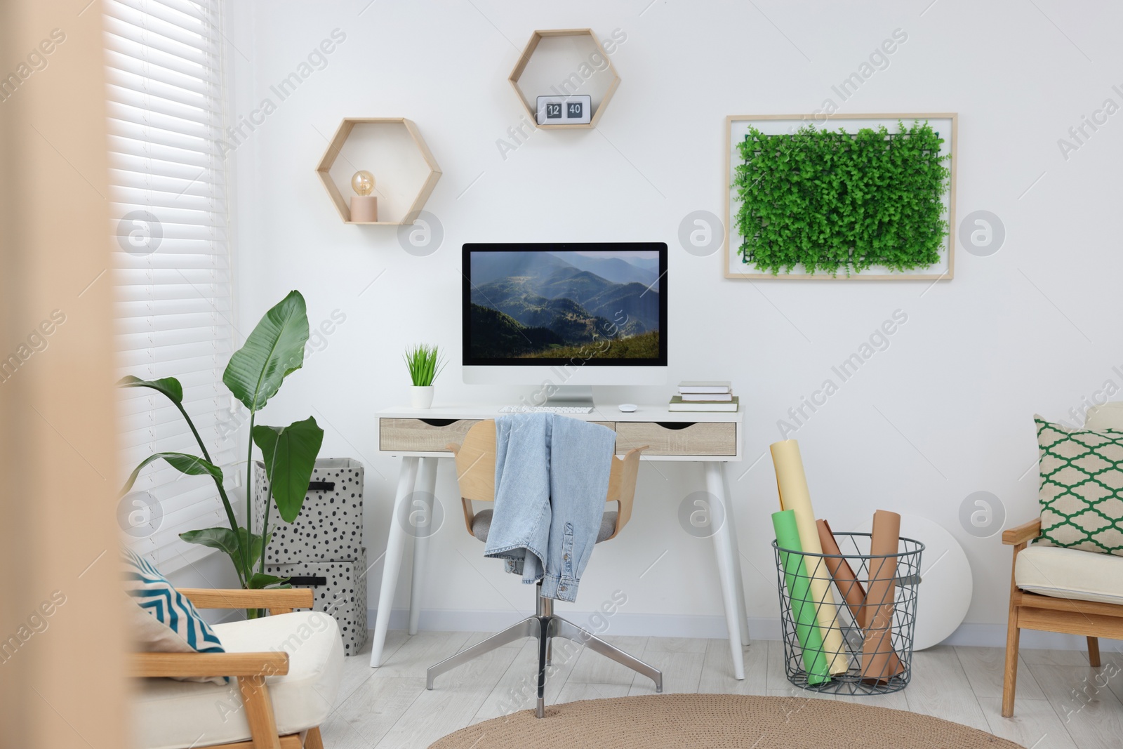 Photo of Green artificial plant wall panel and desk with computer in light room. Interior design