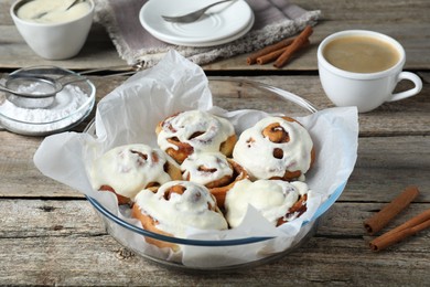 Tasty cinnamon rolls with cream on wooden table, closeup