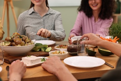 Friends eating vegetarian food at wooden table indoors, closeup