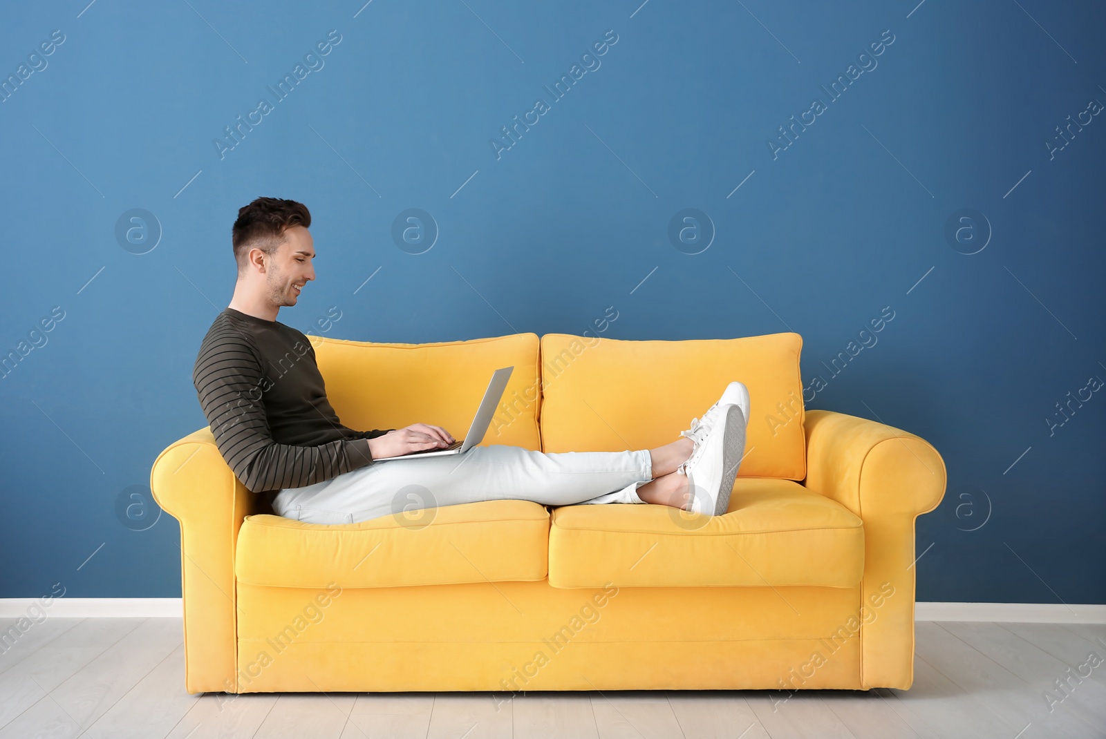 Photo of Handsome young man with laptop on sofa, indoors