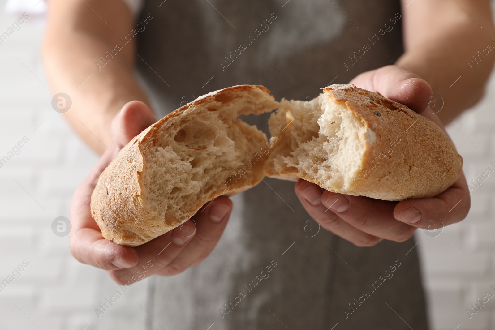 Photo of Man breaking loaf of fresh bread near white brick wall, closeup