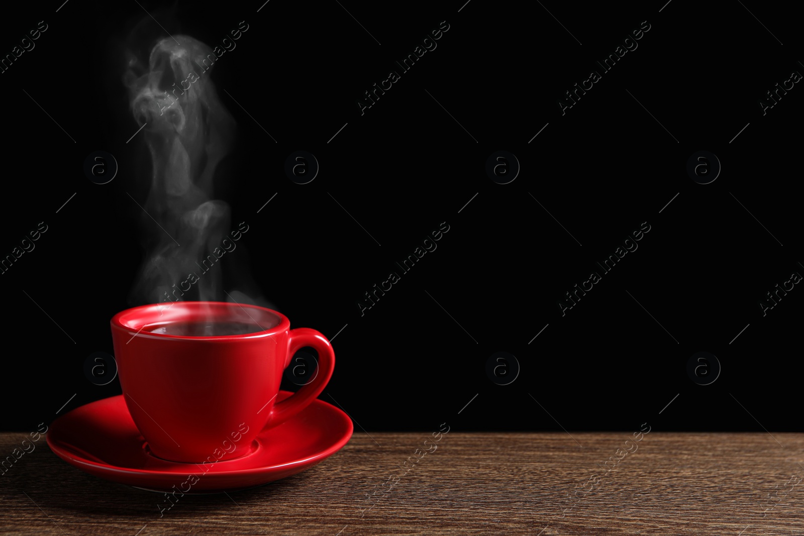 Image of Red cup with hot steaming coffee on wooden table against black background, space for text