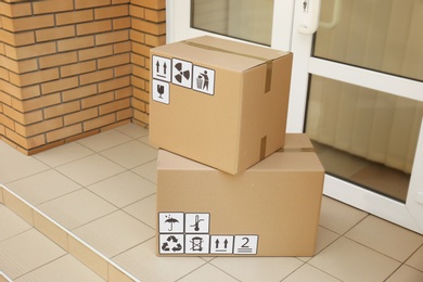 Photo of Cardboard boxes with different packaging symbols on floor near entrance. Parcel delivery