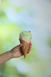 Photo of Woman holding waffle cone with cotton candy on blurred background, closeup