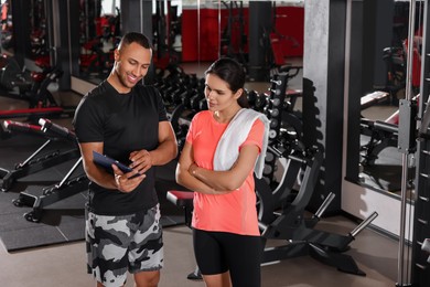 Happy trainer showing young woman workout plan in modern gym, space for text